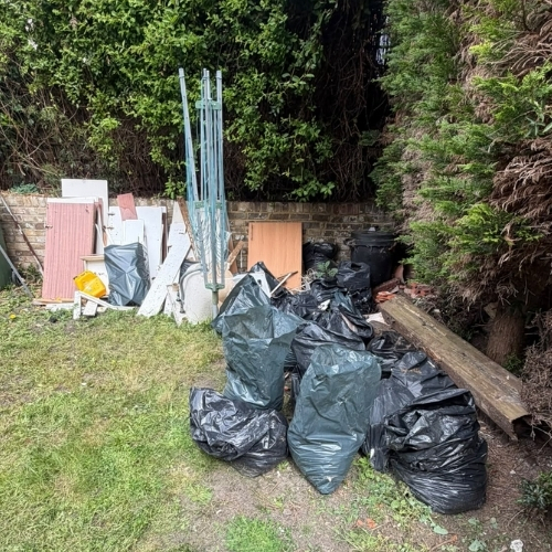 Garden with black waste bags, timber and dismantled panels ready for removal during a Morris Movers garden clearance in Thanet.