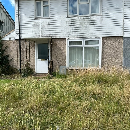 Overgrown front garden with long grass outside a residential property before a Morris Movers garden maintenance service in Thanet.
